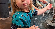 Athena is registered to the contest to win money with this photo: child, children, water_fountain, indoor, playing, curious, blonde, brown_hair, blue_shirt, green_shirt, water, splash, hands, face, expression, candid, fun, activity, young, people