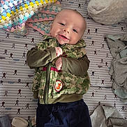 Caspian joined the competition — help win amazing prizes! baby, infant, smiling, camo_jacket, navy_pants, blanket, sock, crib, patterned_mattress, lying_down, cute, child, indoors, soft_toys, fabric, happy, portrait, small_child, clothing, baby_clothes