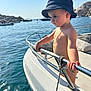 bare_chest, boat, child, daytime, hat, holiday, metal_rail, nautical, necklace, ocean, outdoor, portrait, rock, rope, sky, summer, sunlight, toddler, vacation, water