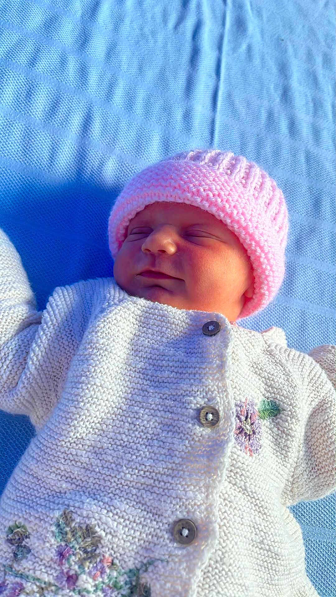 Ivy Rae joined the competition — help win amazing prizes! baby, newborn, pink_hat, knitted_sweater, floral_embroidery, blue_blanket, sleeping, peaceful, closeup, soft_light, child, infant, portrait, cozy, cute, warm_clothing, outdoor, texture, buttoned_sweater, resting