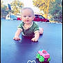 baby, backyard, basketball_hoop, car, child, crawling, curious, cute, daylight, fence, green_shirt, heart_doodle, outdoor, playtime, portrait, smiling, sunny, toy_car, trampoline, trees