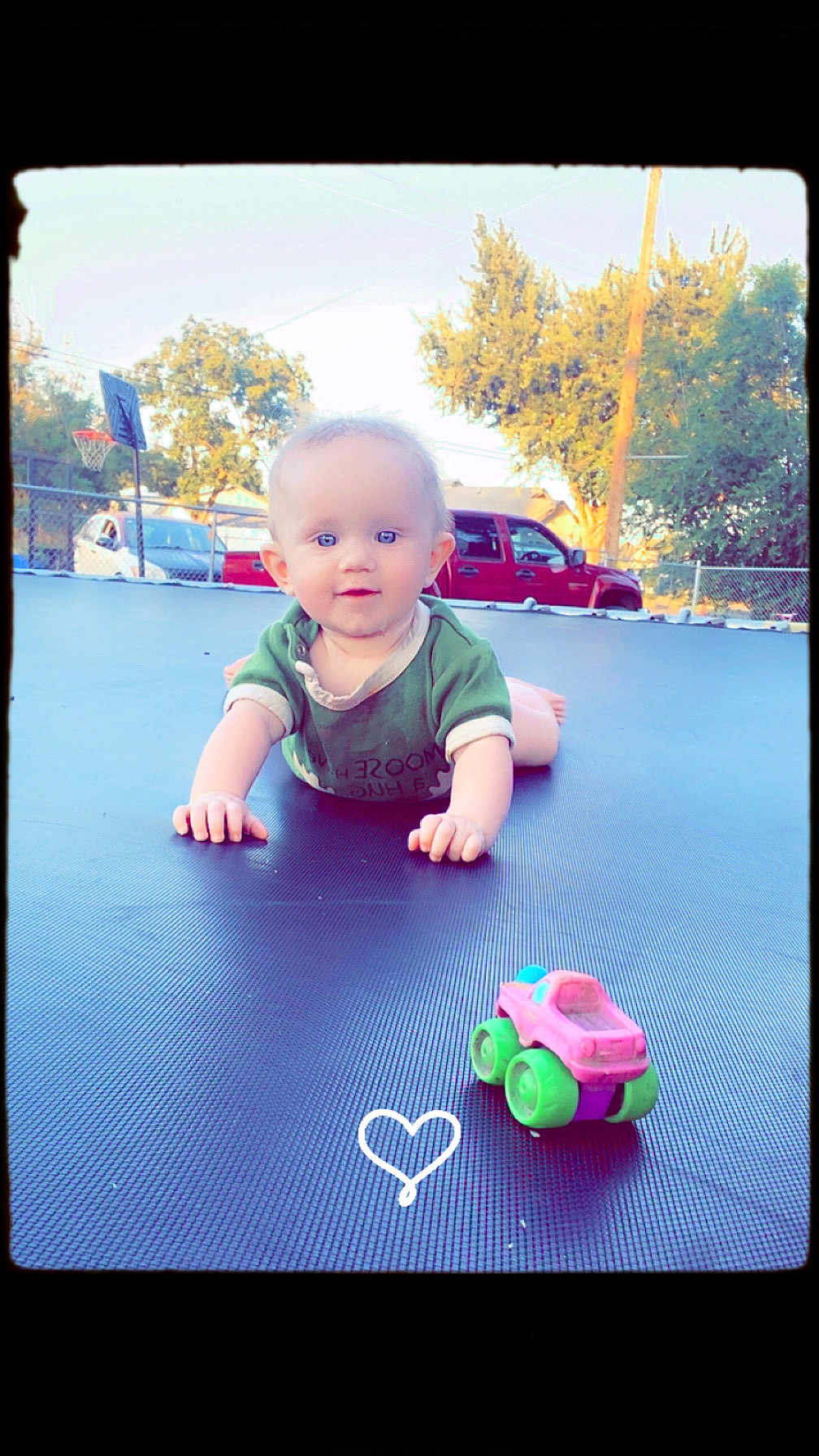Lunna Rose joined the competition — help win amazing prizes! baby, child, trampoline, toy_car, outdoor, green_shirt, crawling, smiling, backyard, trees, basketball_hoop, car, daylight, fence, curious, playtime, cute, heart_doodle, sunny, portrait