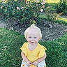 toddler, child, smiling, yellow_top, floral_skirt, blonde_hair, blue_eyes, grass, garden, roses, flowers, outdoor, sunlight, greenery, nature, cute, happy, portrait, standing, summer