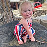 toddler, child, outdoor, rock, tree, red_car, brick_wall, smiling, face, person, short_hair, barefoot, patriotic_clothing, blue_eyes, sunlight, nature, cute, playful, young_child, summer
