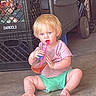 child, toddler, blonde_hair, pink_shirt, green_shorts, plastic_cup, pink_straw, sitting, concrete_floor, crate, darigold, indoor, curious, barefoot, messy_hair, casual, drink, person, young_child, everyday_life