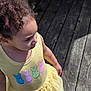 child, toddler, yellow_dress, bunny_patches, curly_hair, outdoor, wooden_floor, sunlight, shadow, side_view, casual_clothing, cute, young_girl, daylight, summer, colorful, playful, innocence, portrait, person