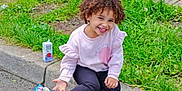 Miracle joined the competition — help win amazing prizes! child, curly_hair, smiling, sitting, curb, street, grass, juice_box, snack_bag, sneakers, pink_sweater, black_leggings, outdoor, daytime, residential_area, deflated_inflatable, happy, casual, person, sidewalk
