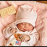 baby, sleeping, pink, hat, blanket, wooden_blocks, teddy_bear_print, clothing, infant, soft_texture, cute, cozy, child, portrait, newborn, resting, indoor, hands, face, babywear
