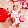 baby, infant, pink_outfit, party_hat, plush_toy, strawberry_toy, cupcake_toy, blanket, soft_texture, celebration, cute, smiling_toy, lying_down, indoors, child, festive, colorful, happy, playful, cozy