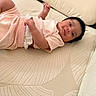 baby, infant, child, pink_clothing, couch, pillow, indoor, portrait, lying_down, smiling, face, skin, hand, home, comfort, cozy, soft_texture, relaxation, cute, young