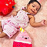 baby, child, pink, plush_toy, stuffed_animal, party_hat, blanket, cute, smiling, infant, soft_texture, celebration, playful, lying_down, indoors, adorable, colorful, toy, clothing, portrait