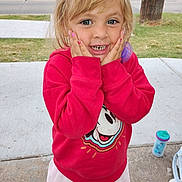 Brandy is registered to the contest to win money with this photo: child, girl, red_sweatshirt, cartoon_character, smiling, hands_on_face, outdoor, sidewalk, grass, road, pacifier, sippy_cup, blonde_hair, blue_eyes, happy, casual_clothing, playful, portrait, cute, young