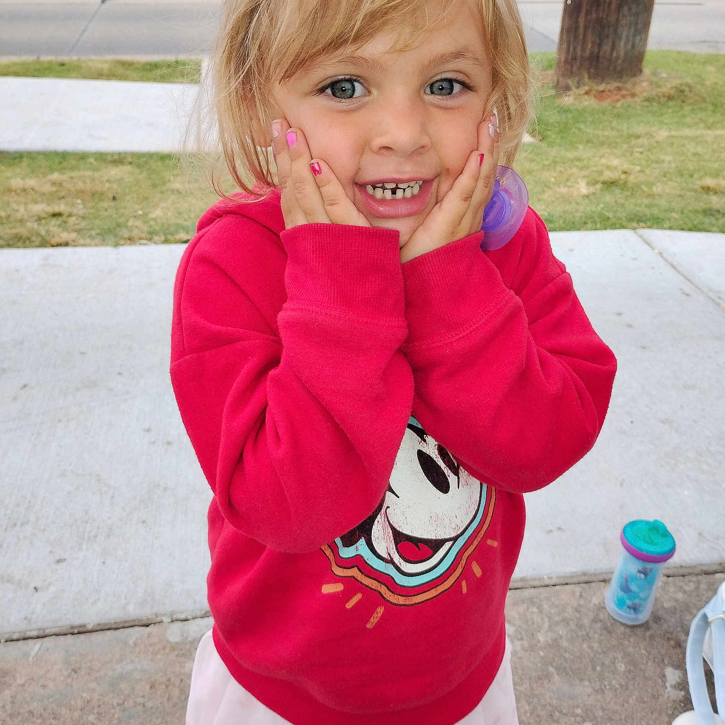 Brandy is registered to the contest to win money with this photo: blonde_hair, blue_eyes, cartoon_character, casual_clothing, child, cute, girl, grass, hands_on_face, happy, outdoor, pacifier, playful, portrait, red_sweatshirt, road, sidewalk, sippy_cup, smiling, young