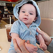 Daniel joined the competition — help win amazing prizes! baby, child, hoodie, blue_clothing, indoor, restaurant, table, drink, straw, adult_hands, cute, portrait, infant, casual, seated, curious, soft_skin, light, face, person