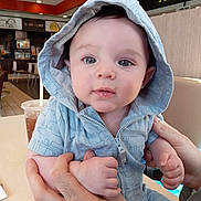 Daniel joined the competition — help win amazing prizes! baby, child, hoodie, blue_clothing, hands, face, eyes, indoor, restaurant, table, drink, cup, person, seated, casual, portrait, cute, infant, holding, expression