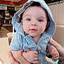 baby, child, hoodie, blue_clothing, hands, face, eyes, indoor, restaurant, table, drink, cup, person, seated, casual, portrait, cute, infant, holding, expression