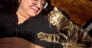 Axel joined the competition — help win amazing prizes! affection, casual, cat, close_up, face, glasses, human, indoor, intimate, lying_down, paw, pet, polka_dot, relaxed, resting, striped_fur, tabby_cat, warm, woman, wooden_background