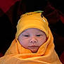 baby, infant, swaddled, blanket, hat, orange, face, cute, newborn, wrapped, child, person, headwear, cozy, portrait, indoors, soft, expression, warm, smile