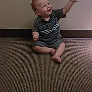 Anthony is registered to the contest to win money with this photo: toddler, child, balloon, red_hair, carpet, indoor, smiling, sitting, shorts, shirt, barefoot, happy, playful, person, young_child, wall, floor, holding, toy, casual
