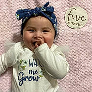 Eliana is registered to the contest to win money with this photo: baby, infant, smiling, headband, white_clothing, blue_flower_pattern, pink_blanket, hand_near_mouth, wooden_sign, five_months, tulle, cute, portrait, happy, child, lying_down, indoors, close_up, face, soft_texture