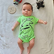 Austin is registered to the contest to win money with this photo: baby, infant, onesie, green_clothing, plush_doll, skull_doll, red_hair_doll, blanket, milestone, wooden_plaque, text, cute, lying_down, infant_face, portrait, celebration, soft_texture, child, two_months, embroidered_text