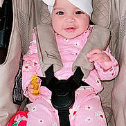 Azariah is registered to the contest to win money with this photo: baby, child, car_seat, pink_clothing, headband, smiling, happy, floral_pattern, straps, safety_harness, infant, cute, indoors, person, young_child, seat, fabric, comfort, portrait, bright