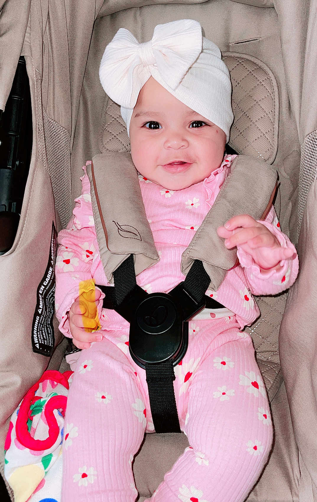 Azariah is registered to the contest to win money with this photo: baby, child, car_seat, pink_clothing, headband, smiling, happy, floral_pattern, straps, safety_harness, infant, cute, indoors, person, young_child, seat, fabric, comfort, portrait, bright