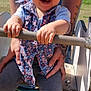 baby, toddler, smiling, laughing, playground, spring_ride, floral_dress, hand_grip, hands, tattoos, bar, legs, leggings, park, grass, sunlight, portrait, seat, adult, closeup