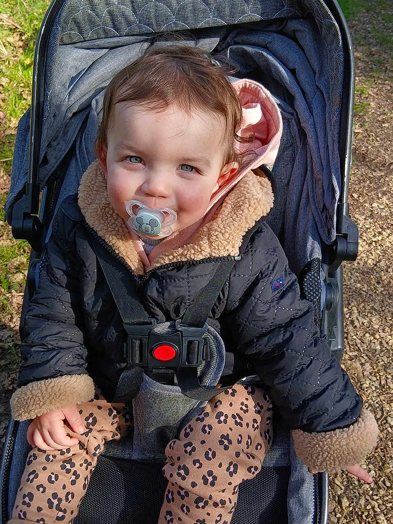 Leïla a rejoint le concours — aidez-le/la à gagner de superbes lots ! child, baby, toddler, pacifier, stroller, jacket, fur_lined_hood, harness, buckle, patterned_leggings, leopard_print, seated, outdoors, park_path, smiling, blue_eyes, hand, brown_hair, sunlight, gravel_path