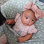 baby, infant, child, pink_bow, headband, floral_outfit, green_cushion, polka_dots, curious, pet_nose, furry, indoor, cute, soft_texture, hand, face, looking_sideways, seated, comfortable, childhood