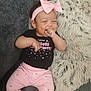 baby, child, infant, pink_bow, headband, black_shirt, pink_pants, stars_pattern, thumb_sucking, smiling, couch, gray_couch, fluffy_pillow, indoor, cute, happy, sitting, cozy, clothing, person