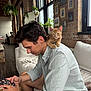 brick_wall, casual_clothing, cat, couch, framed_pictures, home, indoor, kitten, man, modern_interior, natural_light, pet, phone, plant, relaxed, seated, shoulder, watch, window, wood_floor