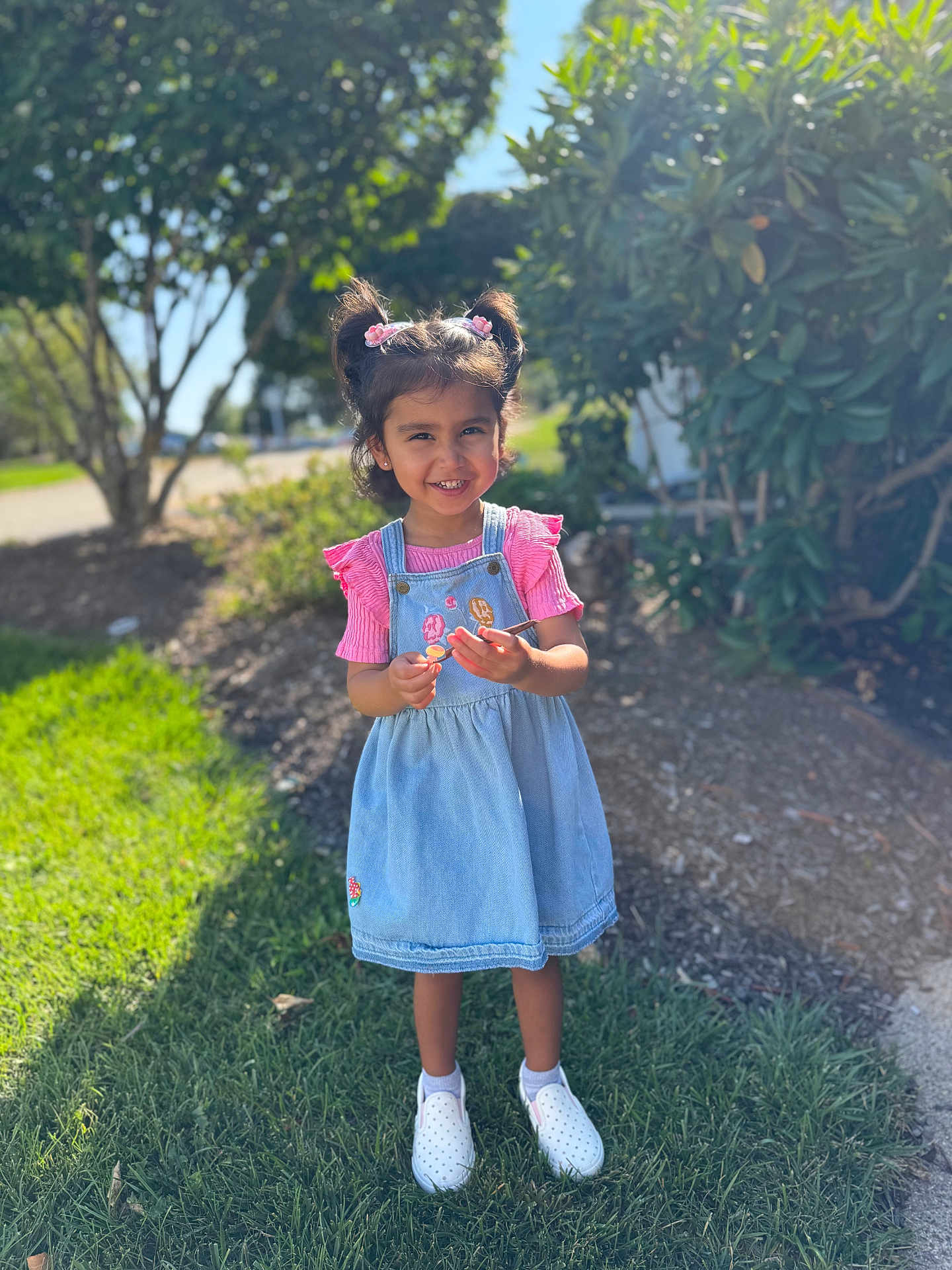 Anshika joined the competition — help win amazing prizes! child, girl, smiling, outdoor, sunlight, grass, trees, pink_clothing, denim_dress, pigtails, hair_accessories, white_shoes, happy, nature, daylight, portrait, young_child, standing, casual_clothing, playful