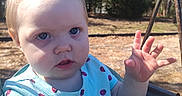Maria is registered to the contest to win money with this photo: baby, blue_eyes, child, curious, daylight, expression, face, hand, ladybug_pattern, nature, outdoor, person, playground, seat, shirt, short_hair, sunlight, swing, toddler, trees