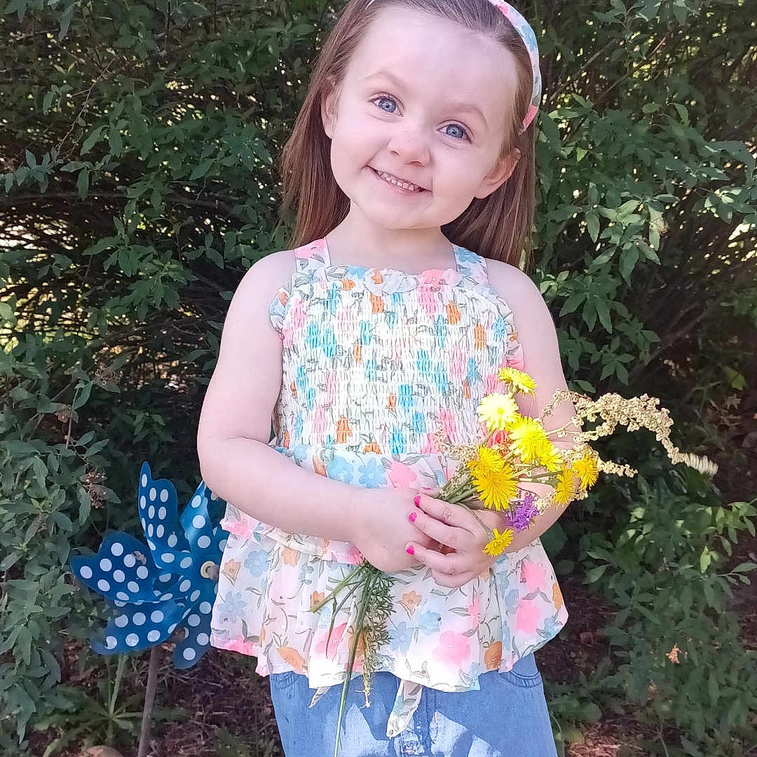 Scarlett is registered to the contest to win money with this photo: blouse, child, clothing, dress, face, female, flower, flowerarrangement, flowerbouquet, girl, grass, head, person, petal, photography, plant, portrait, pottedplant, shorts, vegetation