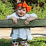 toddler, child, outdoor, greenery, wooden_fence, headband, orange_bow, white_shirt, pumpkin_pants, smiling, hands, grass, nature, sunlight, cute, fall_theme, playful, person, portrait, happy