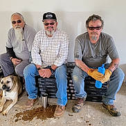 Milo is registered to the contest to win money with this photo: beard, boots, cap, casual_clothing, collar, concrete_floor, construction, dog, flooring_boxes, glasses, indoor, light_wall, men, resting, sitting, smiling, tattoos, water_bottle, work_gloves, worksite