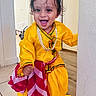 Vivaan is registered to the contest to win money with this photo: bright_colors, child, curly_hair, cute, doorway, face, floor, happy, home, indoor, jewelry, person, playful, portrait, red_and_white_cloth, smiling, toddler, traditional_outfit, wall, yellow_clothing