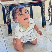 Vivaan is registered to the contest to win money with this photo: baby, barefoot, black_table, child, crawling, crocodile_print, curious, cute, floor_tiles, furniture, gold_detail, home_interior, indoors, looking_up, marble_floor, onesie, playful, short_hair, toddler, young_child