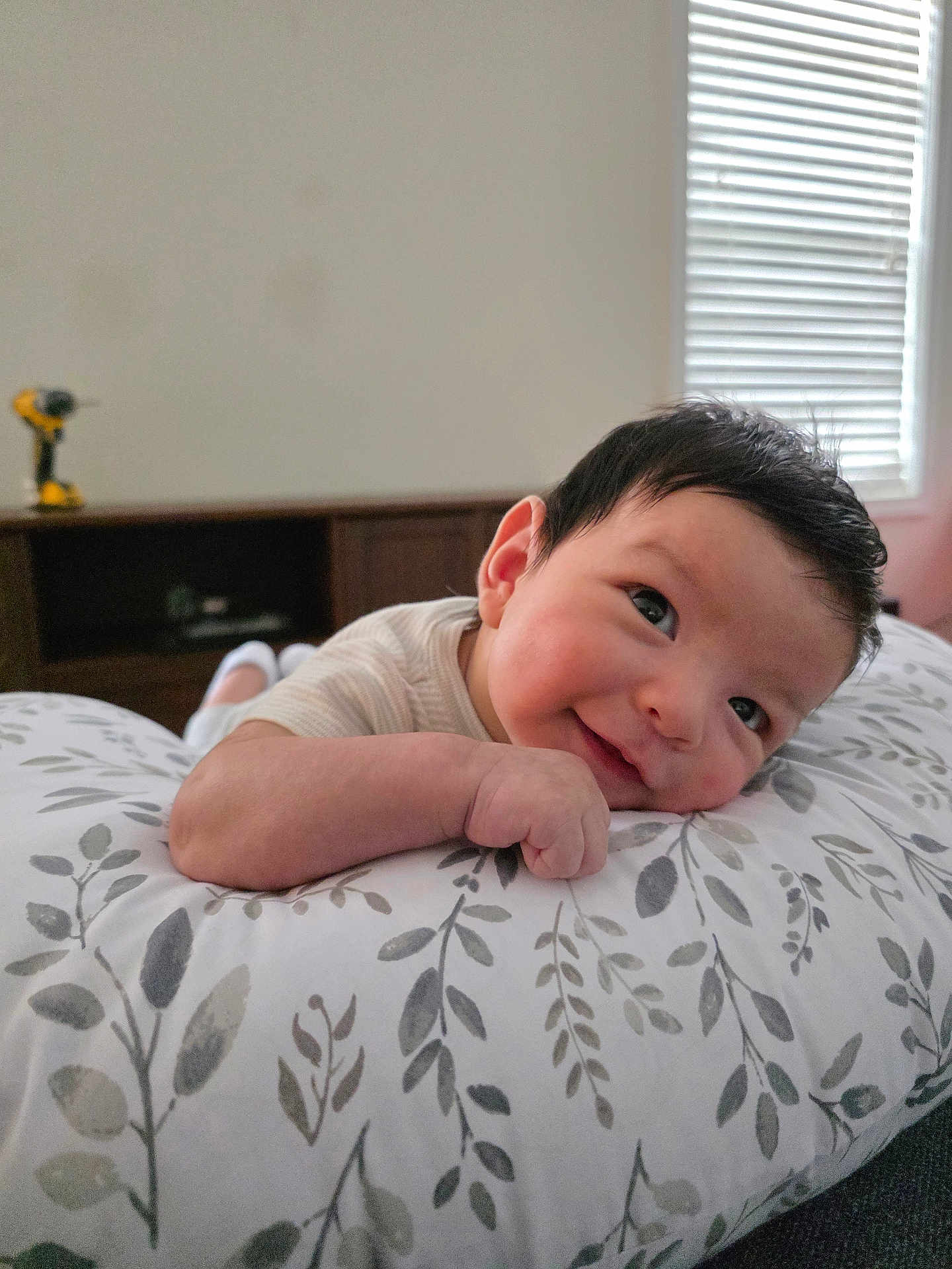 Theodore joined the competition — help win amazing prizes! baby, smiling, pillow, indoor, child, face, curly_hair, resting, cute, infant, patterned_pillow, window, blinds, soft_light, cozy, happy, person, young_child, closeup, portrait