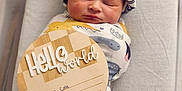 Nolan is registered to the contest to win money with this photo: newborn, baby, infant, swaddle, hat, sleeping, bassinet, milestone_sign, wooden_sign, hello_world_sign, patterned_swaddle, cozy, portrait, closeup, hospital, newborn_photo, peaceful, soft_lighting, cute, newborn_face