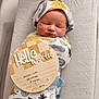newborn, baby, infant, swaddle, hat, sleeping, bassinet, milestone_sign, wooden_sign, hello_world_sign, patterned_swaddle, cozy, portrait, closeup, hospital, newborn_photo, peaceful, soft_lighting, cute, newborn_face