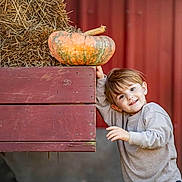 Henry Theodore is registered to the contest to win money with this photo: child, pumpkin, hay, wooden_cart, barn, autumn, smile, playful, outdoor, boy, rustic, fall, clothing, casual, head, face, person, nature, seasonal, daylight