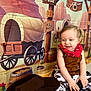 Kayron a rejoint le concours — aidez-le/la à gagner de superbes lots ! child, baby, toddler, bandana, red_bandana, cowboy_costume, western_backdrop, covered_wagon, wagon_wheel, barrel, hat, smile, sitting, portrait, props, indoor, costume, playful, cute, photography