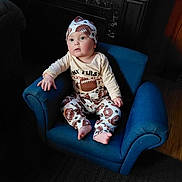Austin is registered to the contest to win money with this photo: baby, child, infant, blue_chair, football_pajamas, hat, indoor, portrait, curious, seated, wooden_floor, cozy, cute, wide_eyes, small_chair, pajamas, clothing, person, furniture, young_child
