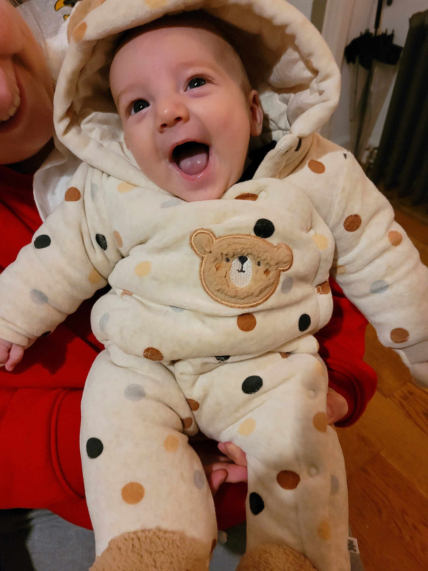 Finn joined the competition — help win amazing prizes! baby, child, smiling, happy, onesie, polka_dots, bear_patch, hooded_clothing, indoor, person_holding, red_clothing, face, expression, warm_clothing, floor, wooden_floor, infant, cute, portrait, cozy