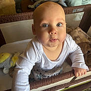 Kaleb is registered to the contest to win money with this photo: baby, child, playpen, toy, blanket, indoor, person, infant, clothing, cute, face, hand, expression, home, furniture, soft_toy, looking_up, curious, standing, light