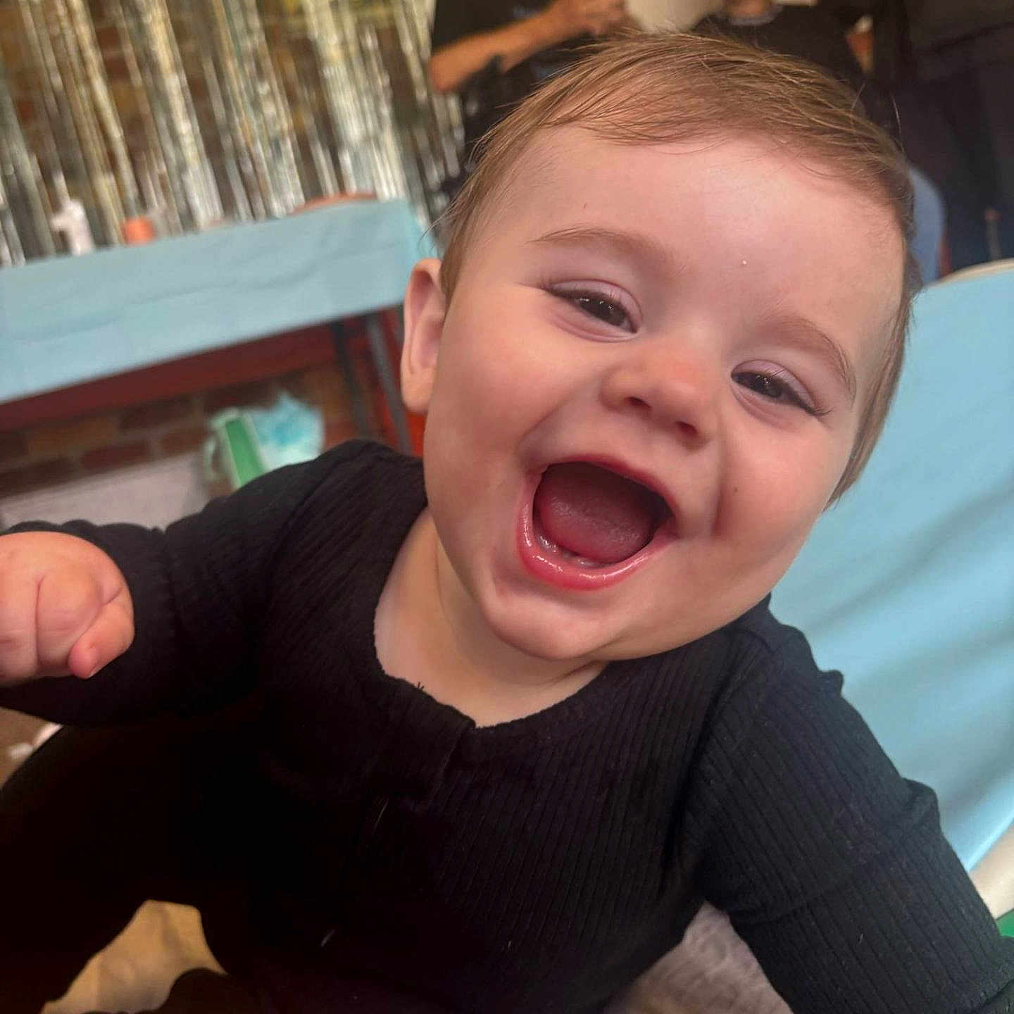 Tahnee is registered to the contest to win money with this photo: baby, black_clothing, blurred_background, cheerful, child, decorations, face, happy, indoor, infant, joyful, mouth_open, party, people_in_background, person, portrait, seated, smiling, table, young_child