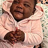 baby, child, smiling, pink_hoodie, curly_hair, indoor, portrait, happy, cute, clothing, infant, hand_gesture, patterned_background, cozy, face, sitting, earrings, baby_clothes, childhood, expression
