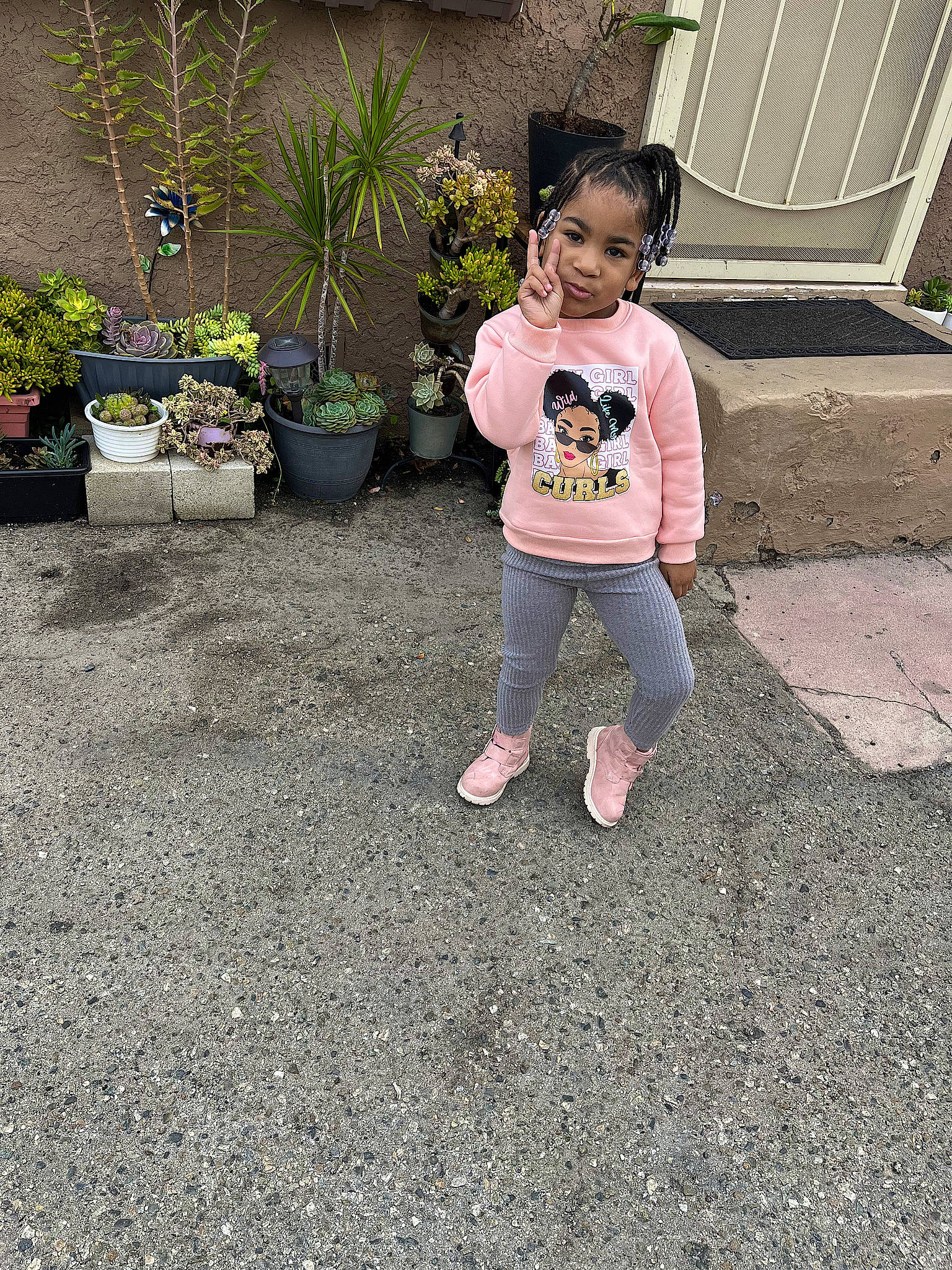 Rayna is registered to the contest to win money with this photo: annual_plant, asphalt, baby_toddler_clothing, child, concrete, flooring, flowerpot, garden, grass, groundcover, houseplant, landscape, leisure, person, plant, road_surface, sidewalk, sitting, soil, t_shirt